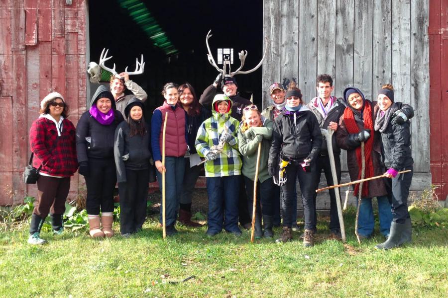 A group of people gather together outside of a barn to pose for a group photo.
