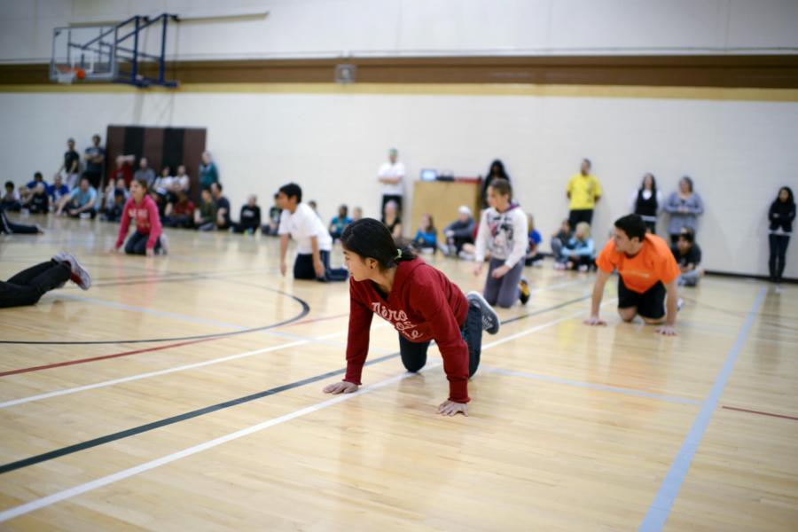 An physical education student leads a class in a gymnasium demonstrating how to perform a pushup.