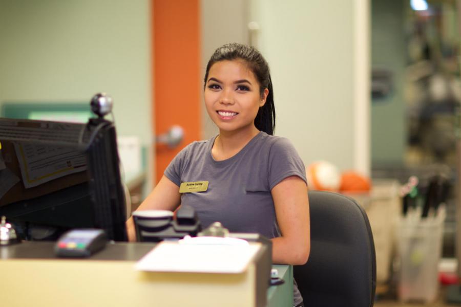 A Faculty of Kinesiology student sits at a work station in front of a computer, she wears a name tag.