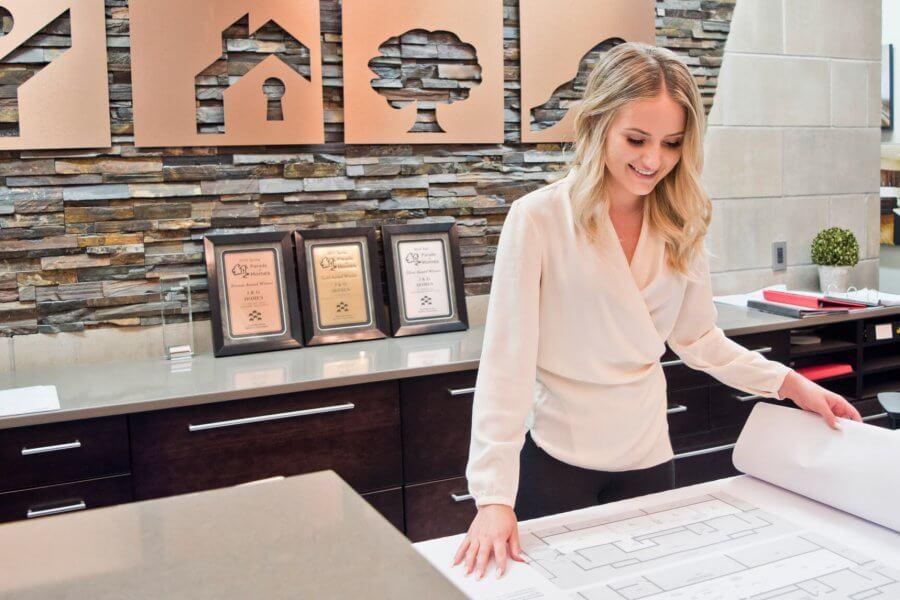 An architecture co-op student stands at a counter, studying a large blueprint of a building.