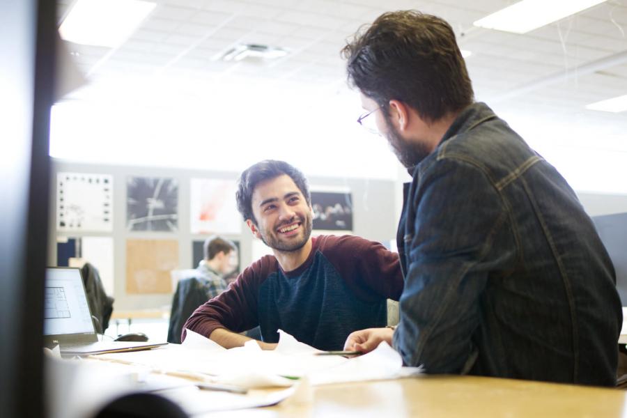 A student smiles while listening to another student speak in a classroom.