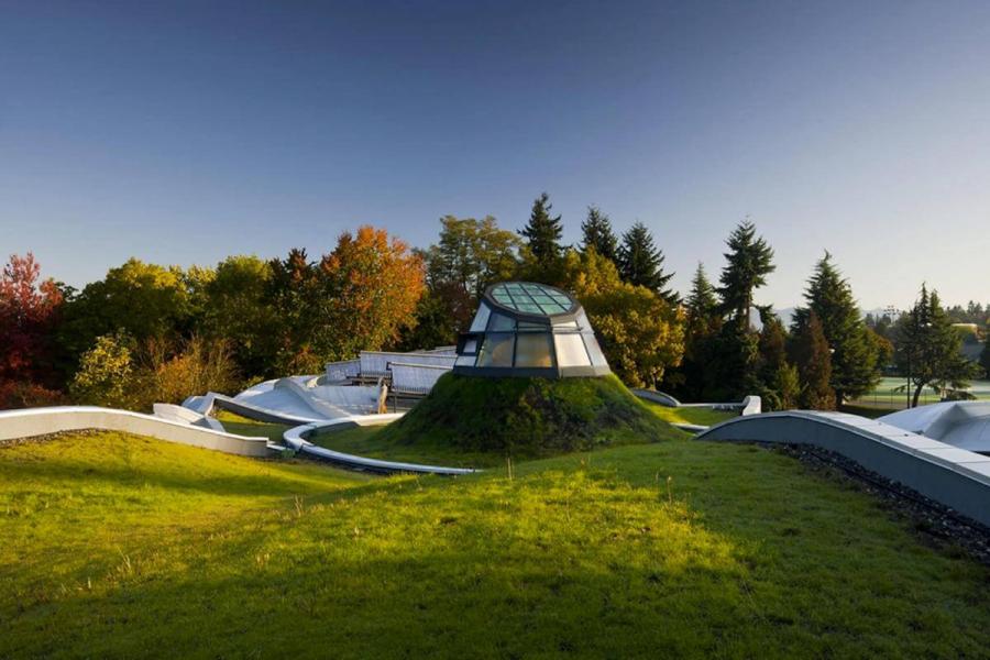 A beautiful landscape with grassy hills, trees and a glass dome structure emerging from under the ground.