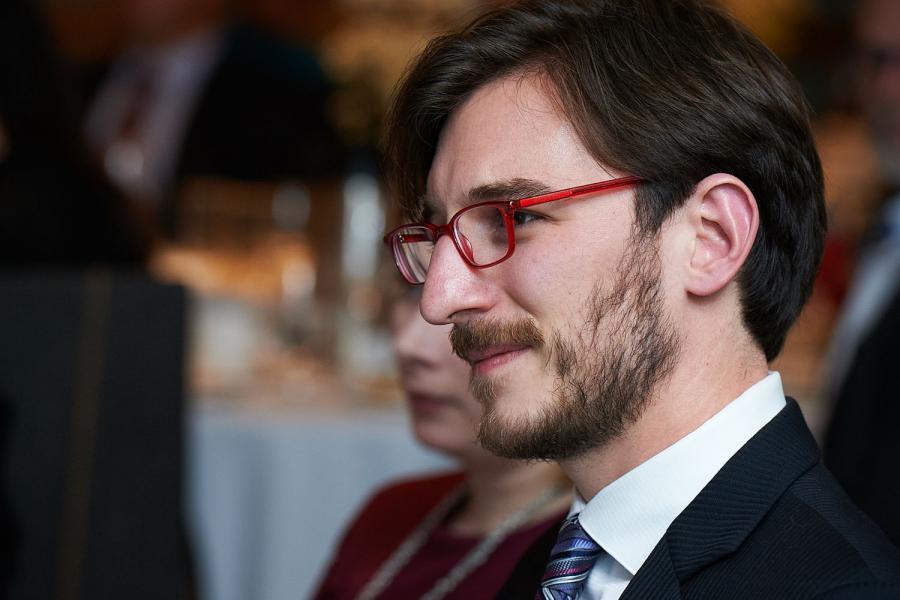 Man white glasses and brown hair in a suite smiling. 