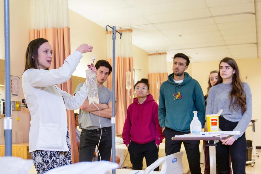 Nursing students stand and watch an IV demonstration. 