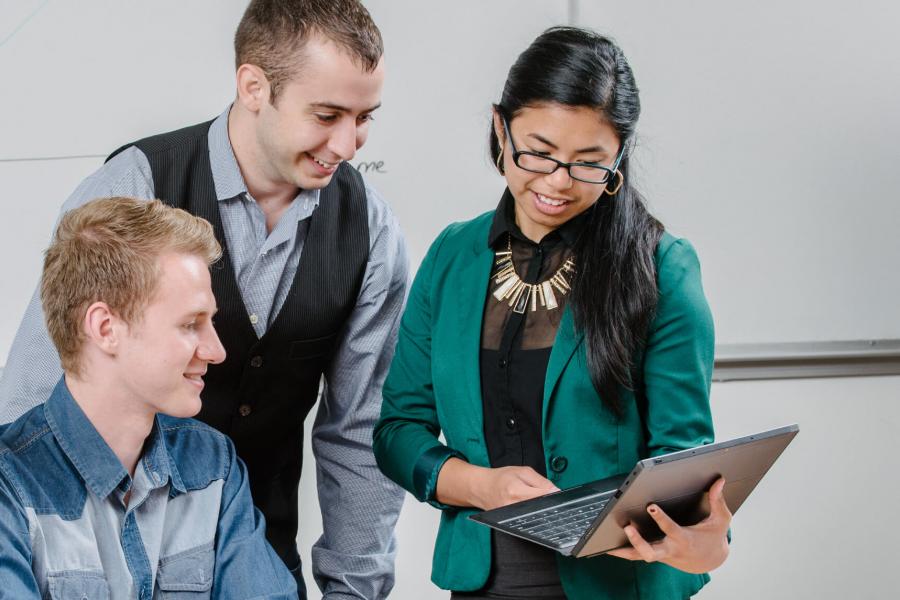 Three people in an office, one holds a laptop and shows the others the screen.