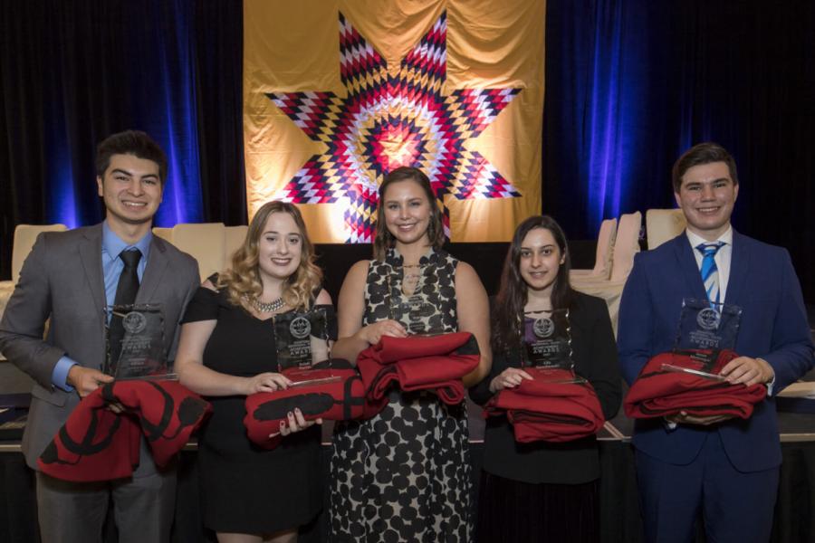 Indigenous Commerce students stand together holding red blankets.