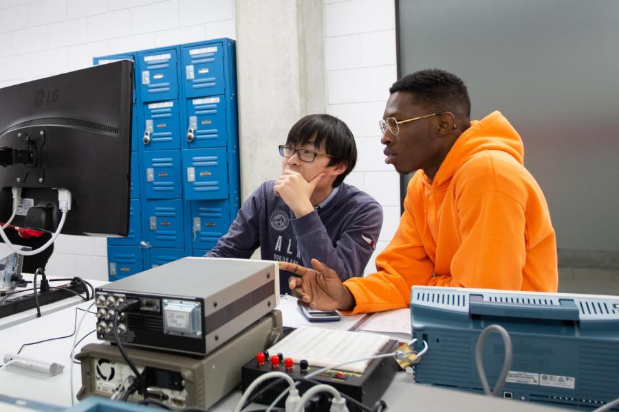 Two engineering students sit at a desk and work together at a computer.