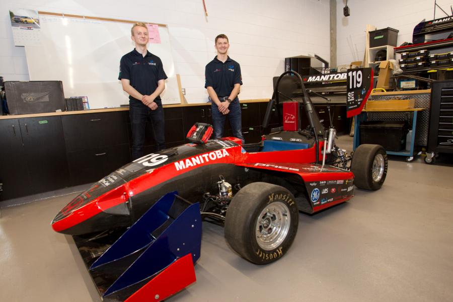 Two mechanical engineering students stand behind a small racing car they have built.