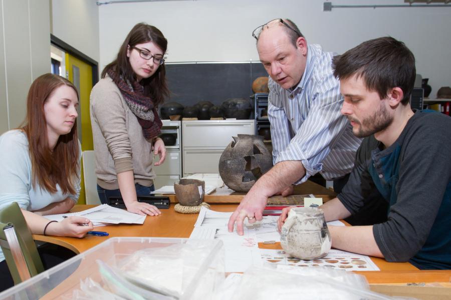 Students work at a table with a professor.