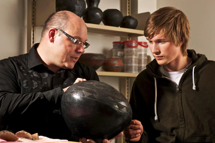 A teacher points out a detail on an artifact to a student.