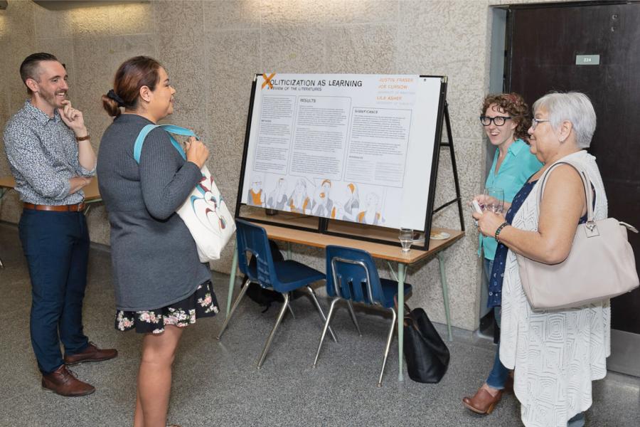 Members of teh Faculty of Education and community members stand and discuss a research display.