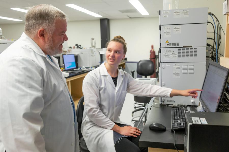 A student and a researcher look at a computer monitor.