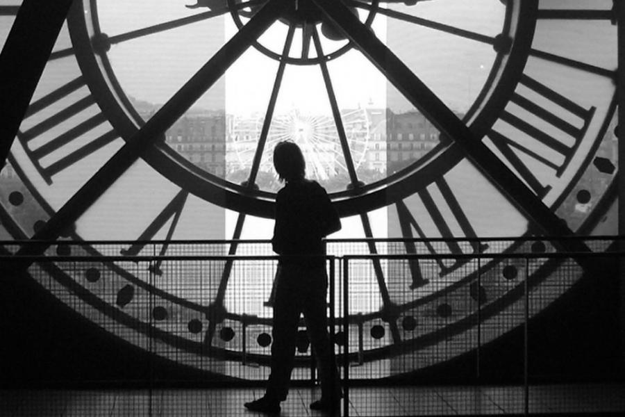 A black and white images of a person standing behind a large clock.