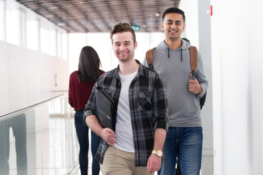 Two smiling students walk down a hallway.