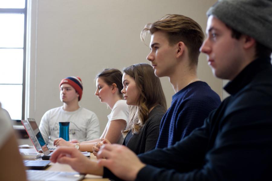 Five students seated in a row listen attentively during class.