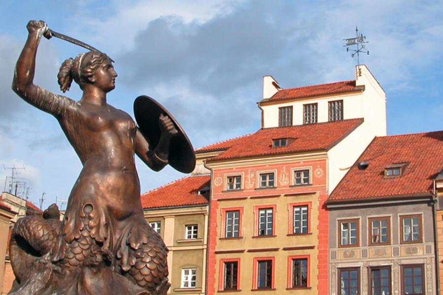 A statue with a row of buildings behind it in Warsaw, Poland. 