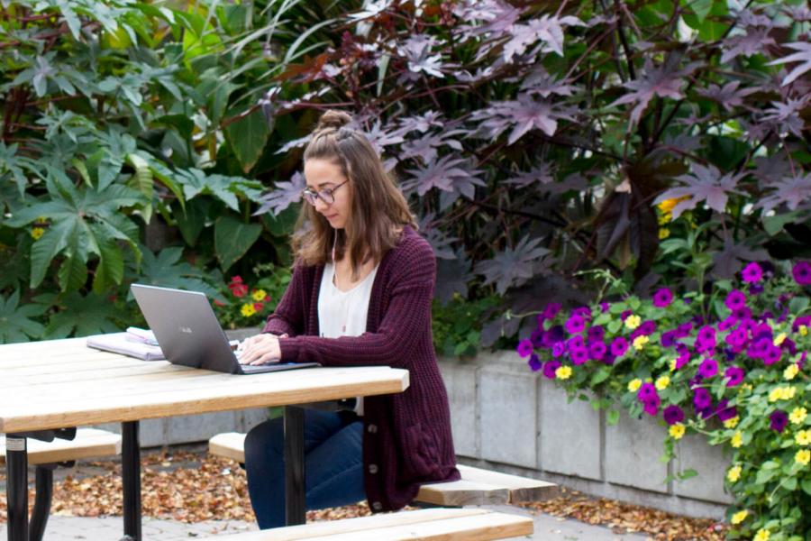 A student works on a laptop while seated at an outdoor picnic table.