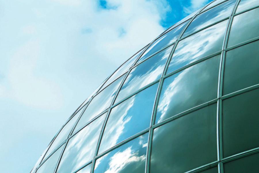 A round glass building with the blue sky and clouds reflected in the glass.