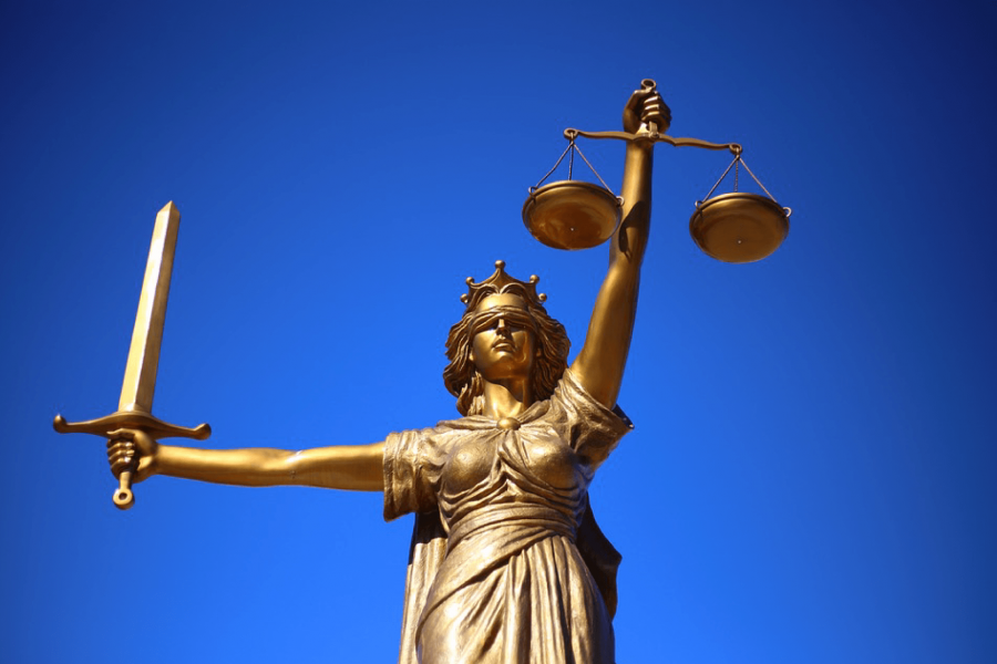 A statue of a woman holding a scale and a sword backed by a bright blue sky.