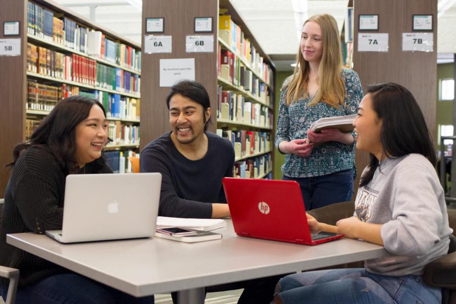 Four students talking together in a library. 