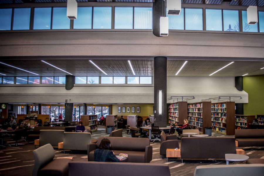 A large open space inside a library with bench seating and students studying.