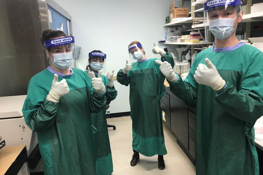 Health Sciences students in full personal protective equipment are standing in a lab, giving a thumbs up to the camera.