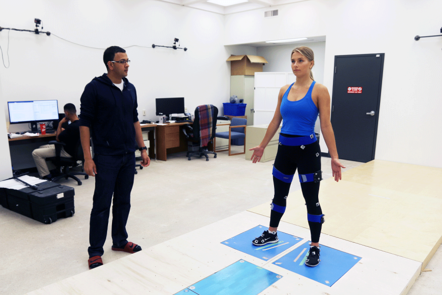 A clinician assesses a patient who is standing with her legs shoulder-width apart.