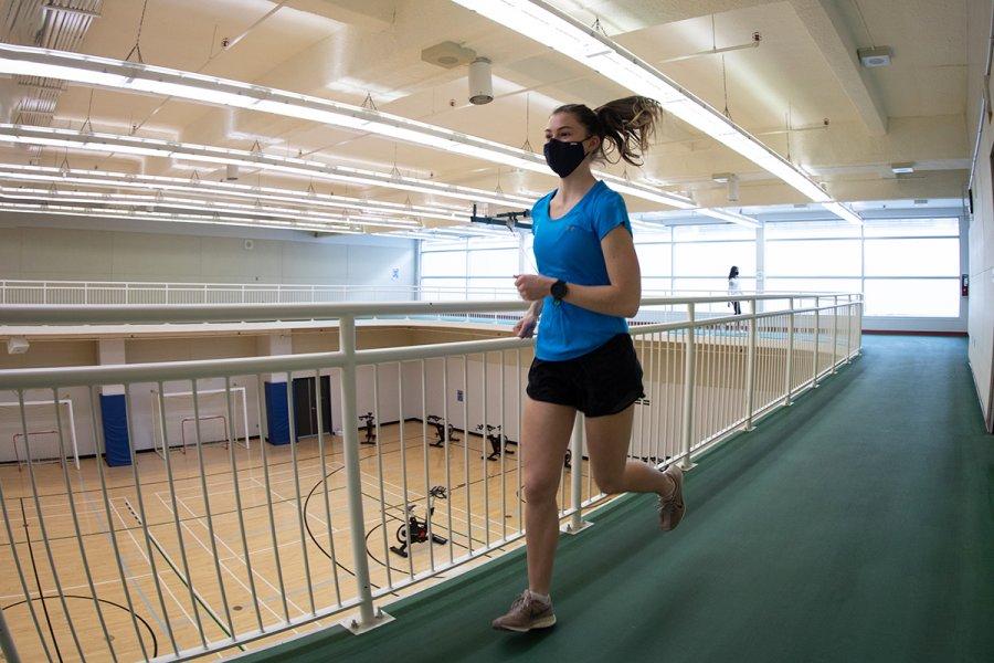 A woman wearing a mask runs around the track inside the Joe Doupe Recreation Centre.