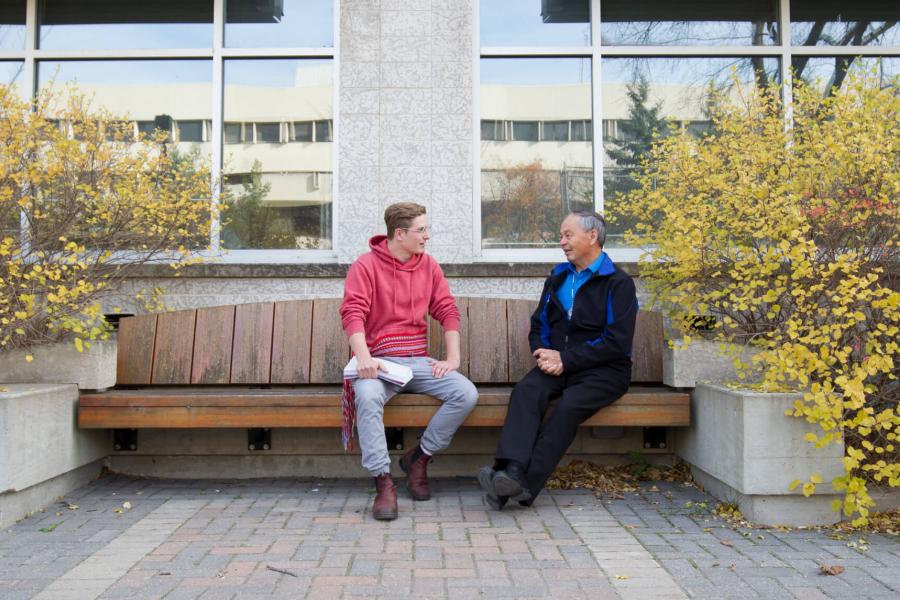 A Metis student sits on a bench and talks with Elder-in-Residence Norman Meade.