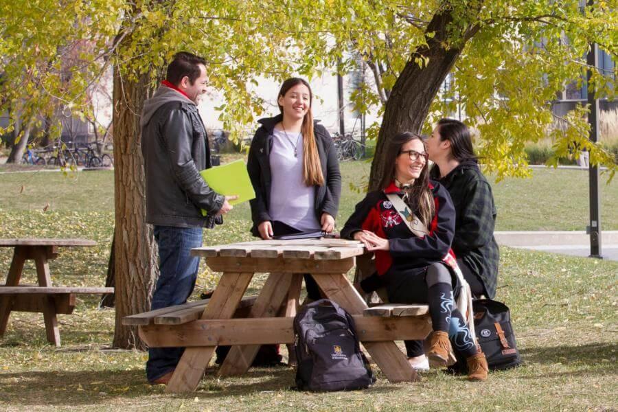 Several Indigenous students sitting together outdoors at a picnic table laughing and talking.