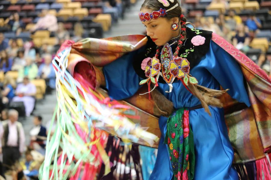 An indigenous student dances in traditional colourful clothing during the graduation pow wow. 