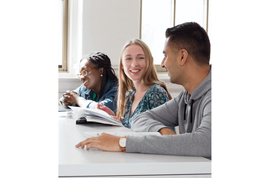 Three students seated at a desk together talking as they work.