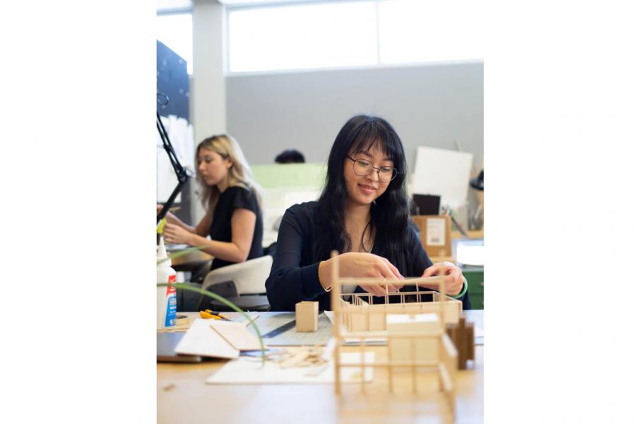 An architecture student carefully works on a project at her desk.