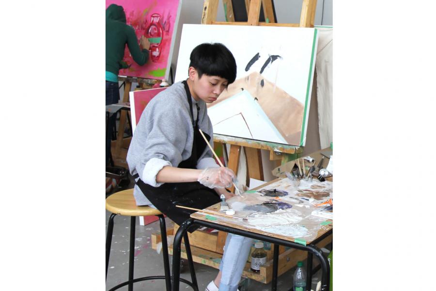 A Faculty of Arts student sits in front of a canvas working on a painting.