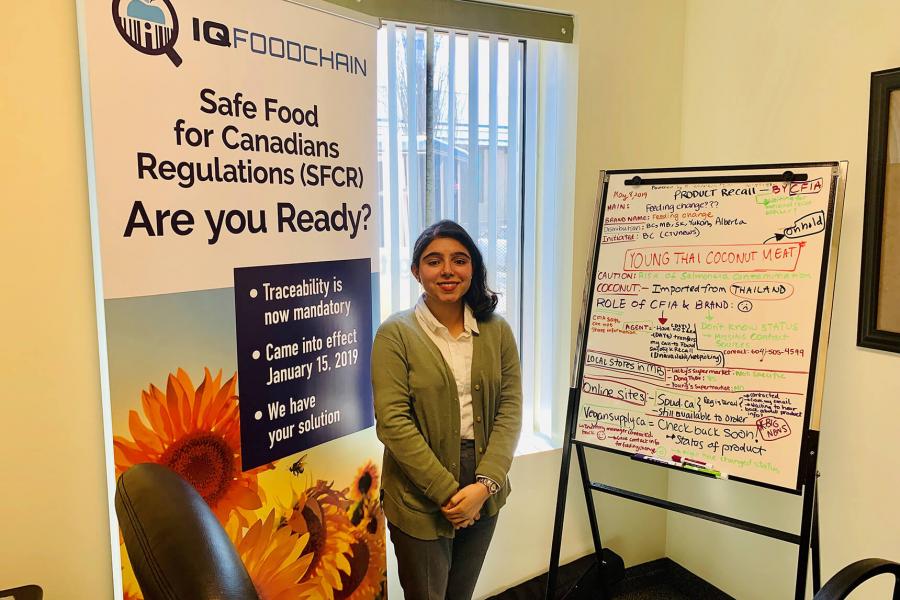 A graduate stands in front of a banner that reads IQ FoodChain.