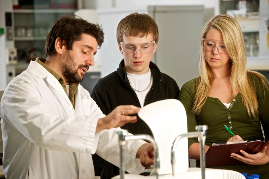 A professor shows two students some equipment in the lab.