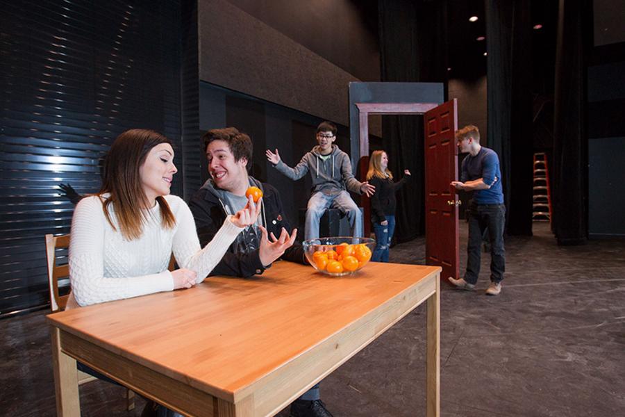 two students rehearsing at a table on stage with a bowl of oranges.