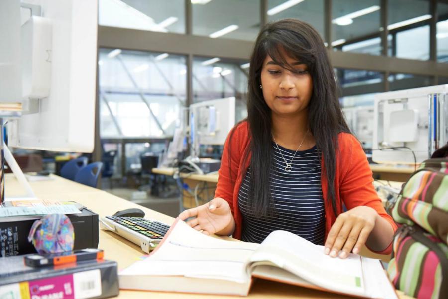 A student working at a desk opens up a book and flips through the pages.