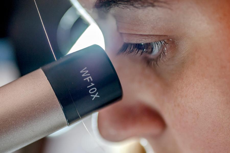 A closeup of a person looking into a microscope.