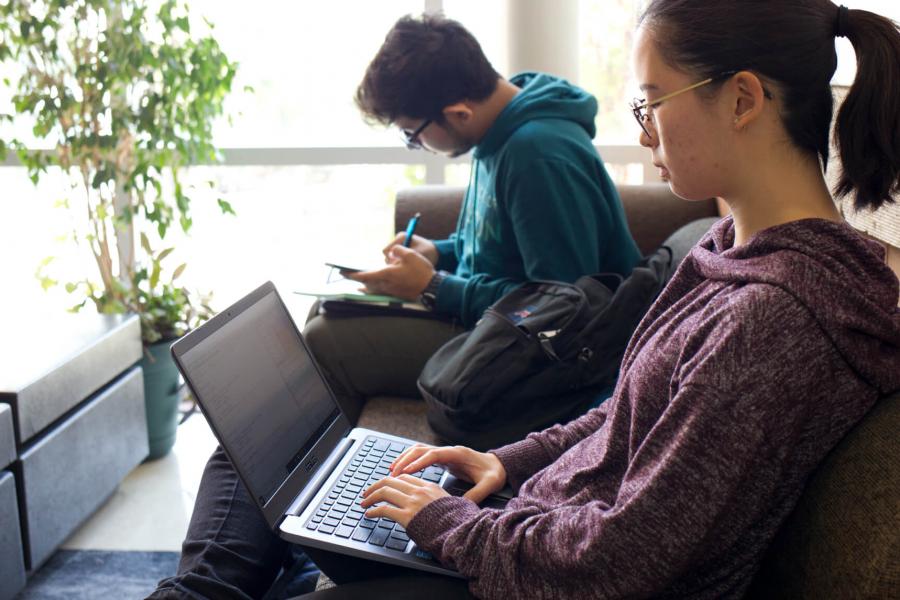 Two students seated side by side working on laptops.