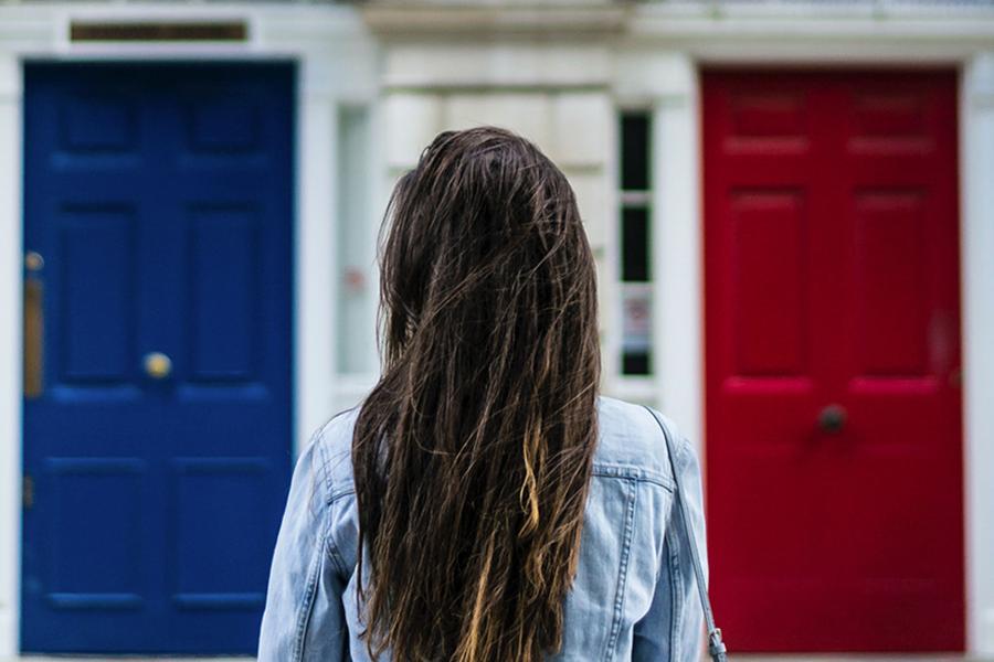 A woman from behind standing in front of two doors, one blue and one red.