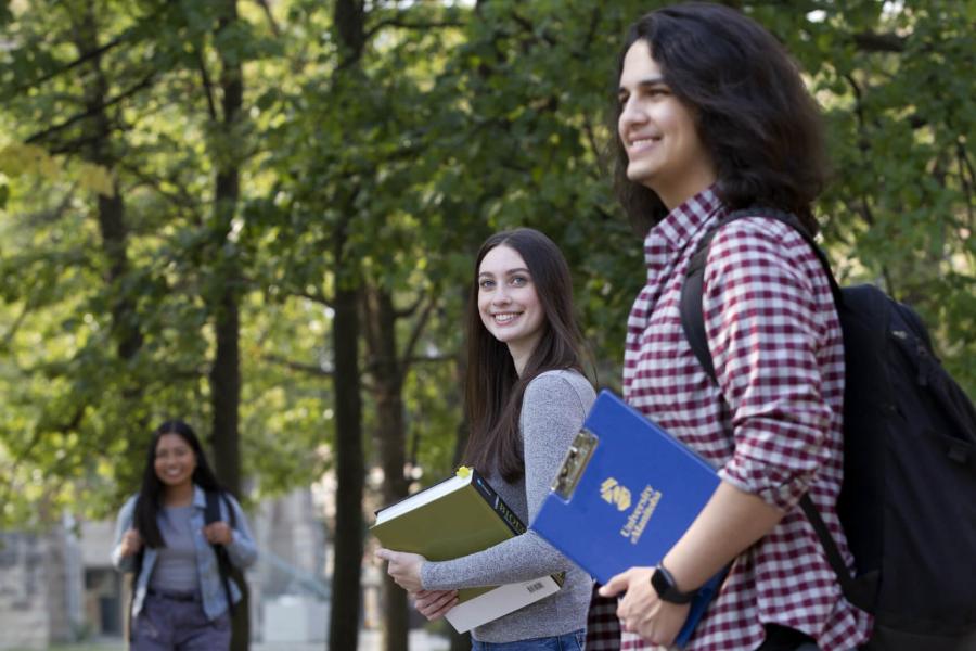 Two students walking together outdoors smiling as they carry their books.