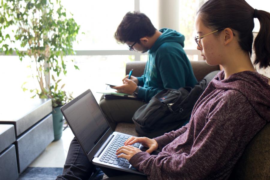 Two students seated beside each other working on laptops.