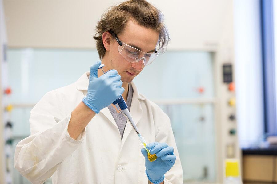 A student using a pipette to transfer a yellow liquid in to a small vial.