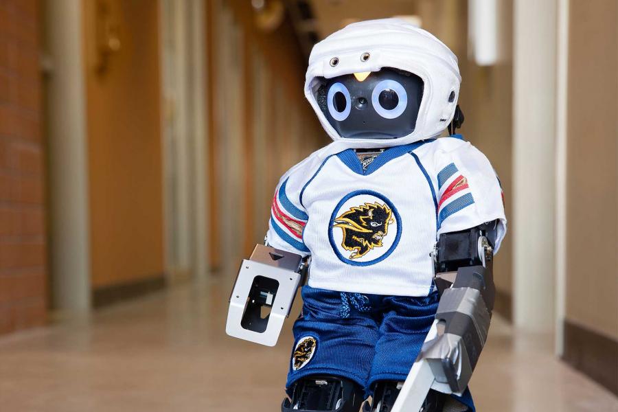A small humanoid robot dressed up in a UM bisons hockey jersey, shorts and helmet.