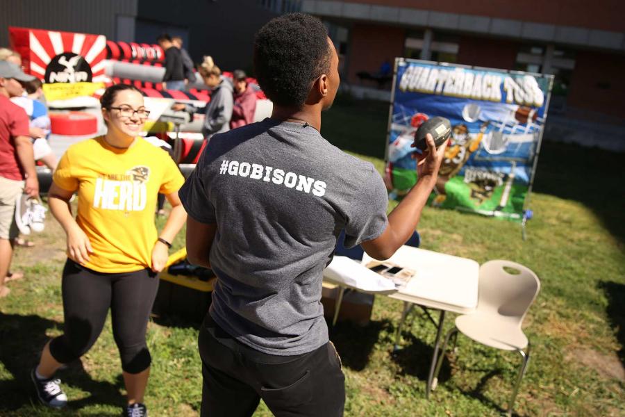 Students wearing UM Bisons t-shirts play carnival games outside.