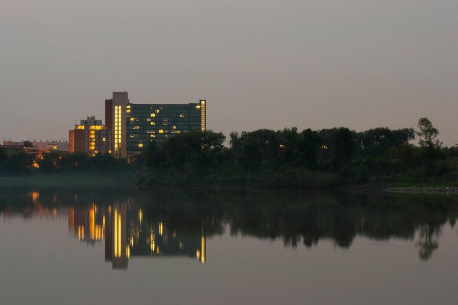 A high-rise apartment building is lit up at night and reflected in the still water of the Red River. 