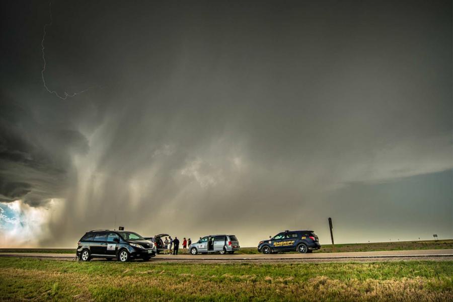 Four vehicles with researchers parked on the side of a road during an intense storm with black clouds and lightning. 