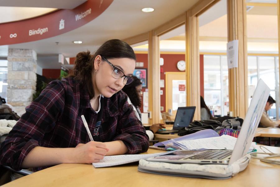 An Indigenous student studies at a table inside Migizii Agamik - Bald Eagle Lodge.