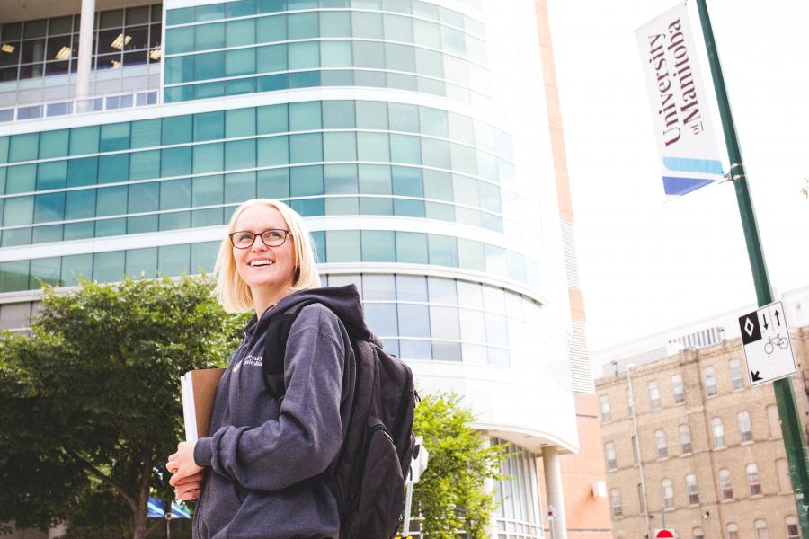 An image of a smiling student, standing outside of UM Bannatyne Campus during summer.